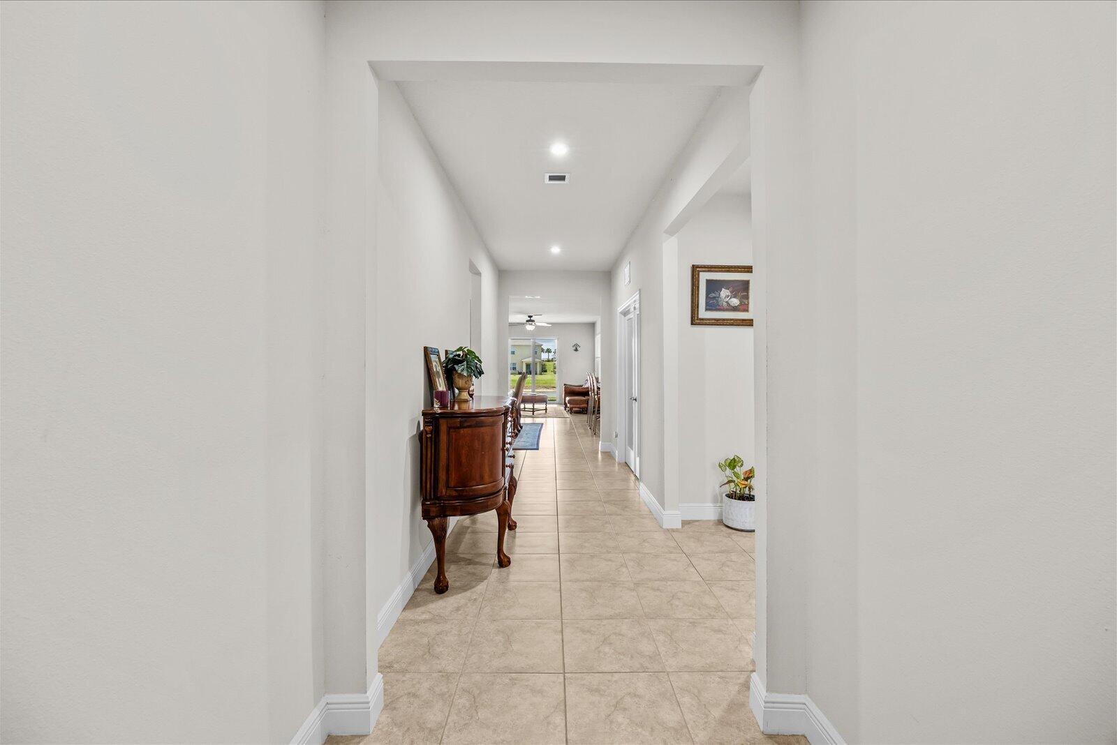 A long hallway with tile flooring leads from a white entryway toward a living area — PORT ST. LUCIE, FL