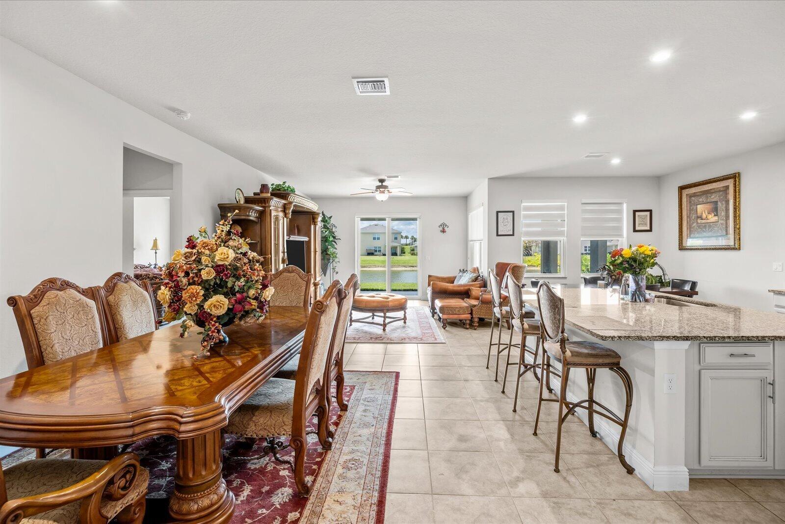 An open-concept dining and kitchen area features a wooden table, island seating, and tile flooring — PORT ST. LUCIE, FL