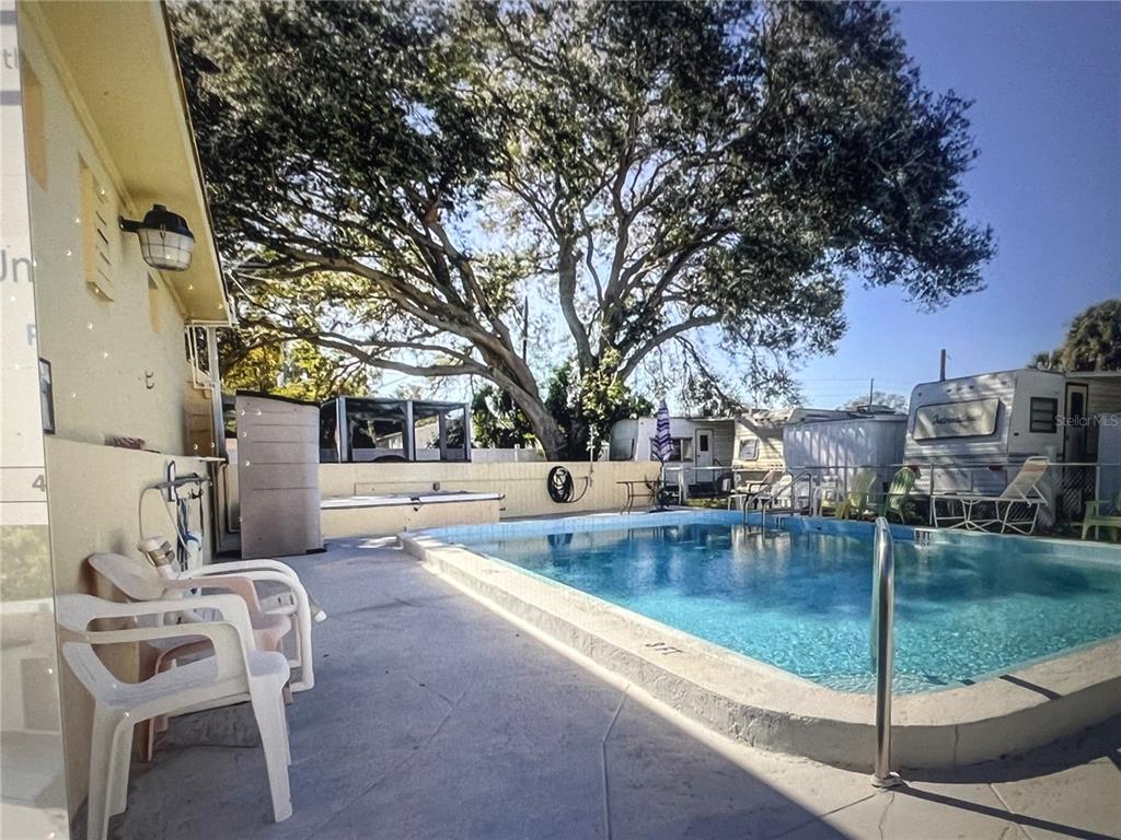 A backyard swimming pool with a concrete deck, patio chairs, and a large oak tree — 4772 67TH WAY N UNIT 51, ST PETERSBURG, FL