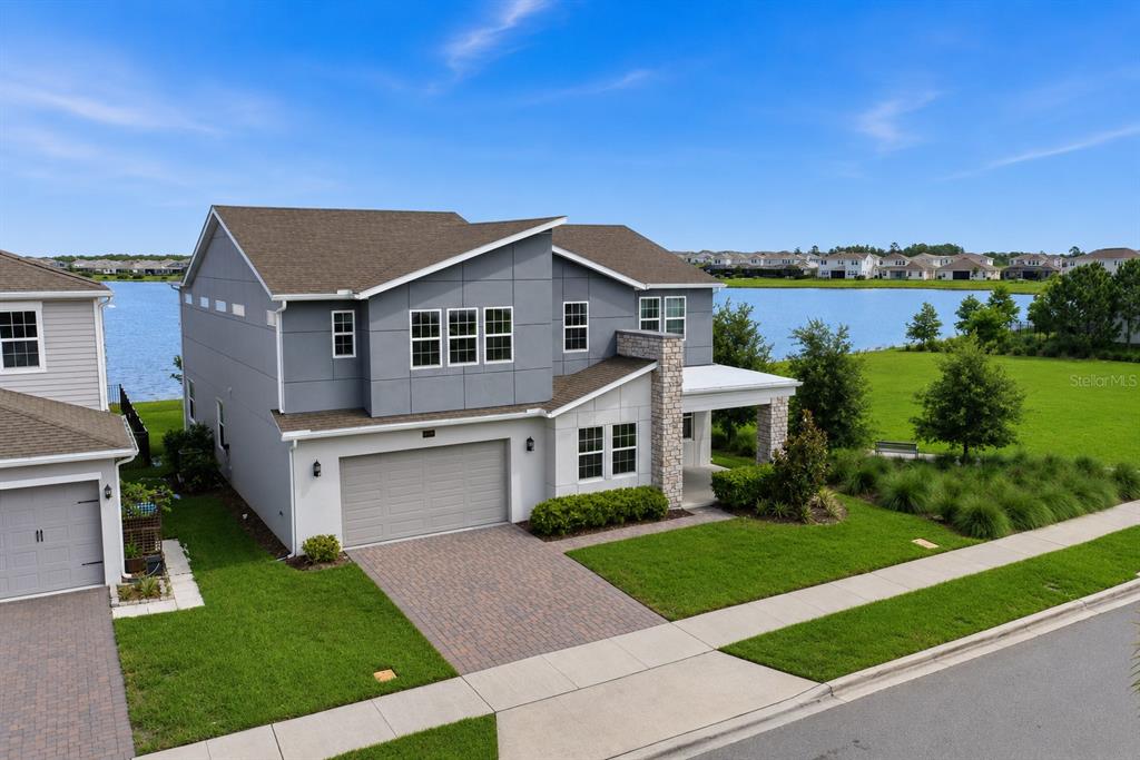A two-story gray house with a stone accent wall and a paved driveway faces a lake — 18387 MOWRY COURT, ORLANDO, FL