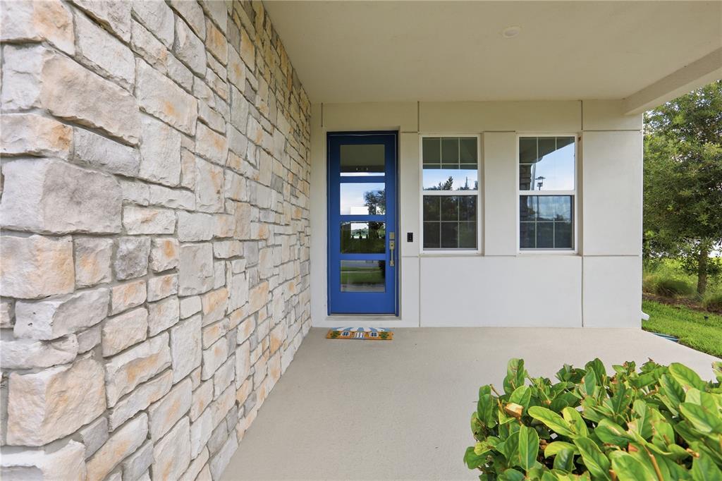 A blue front door stands on a covered porch next to a stone-clad wall — 18387 MOWRY COURT, ORLANDO, FL