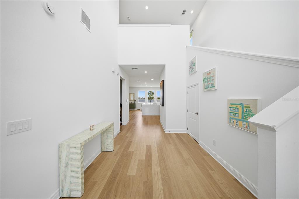 A bright, high-ceilinged entryway features light wood flooring, a console table, and a staircase — 18387 MOWRY COURT, ORLANDO, FL