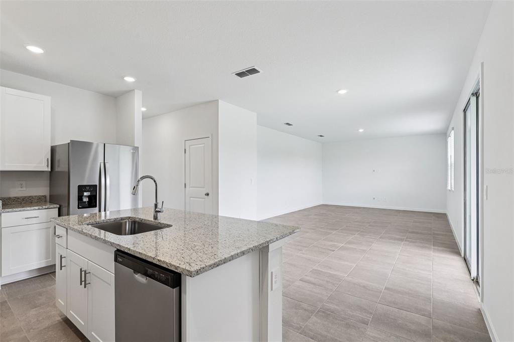 A kitchen with a granite island and stainless steel appliances opens into a tiled living area — 8 WANDERING CREEK WAY, PALM COAST, FL