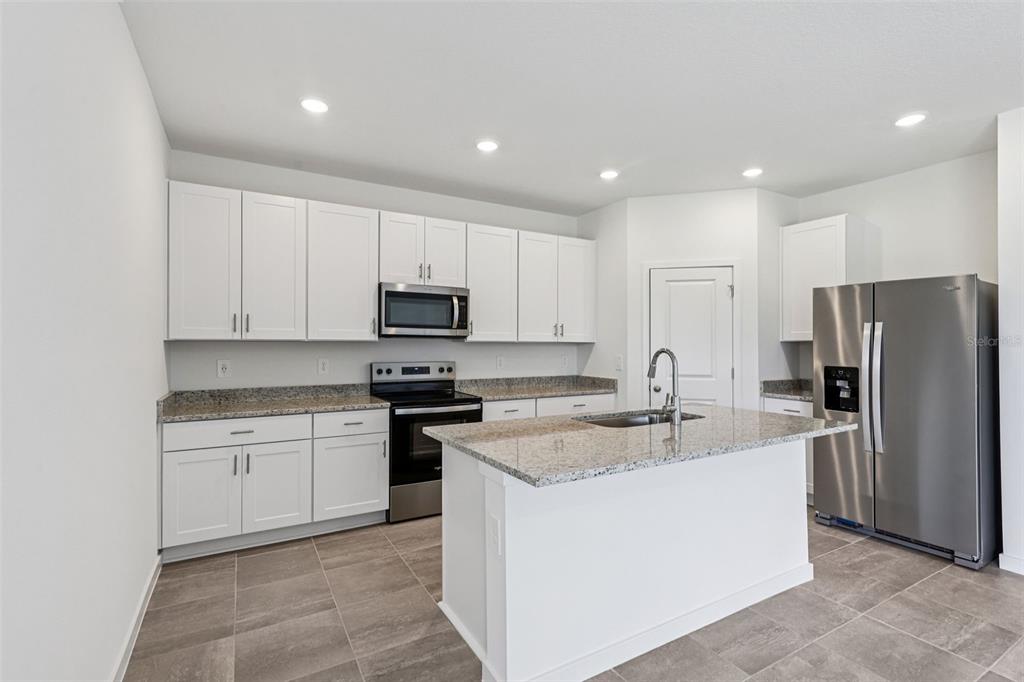 A modern kitchen features white cabinets, granite countertops, stainless steel appliances, and gray tile flooring — 8 WANDERING CREEK WAY, PALM COAST, FL