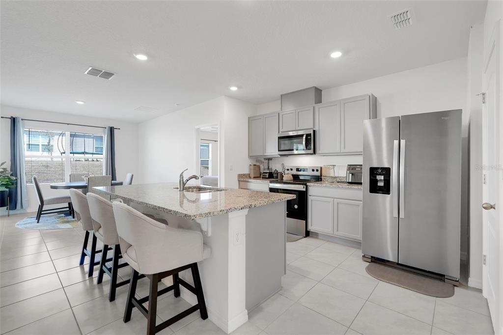 A kitchen features a granite-topped island, light gray cabinetry, and stainless steel appliances — 11400 AMBER RIDGE DRIVE, ZELLWOOD, FL