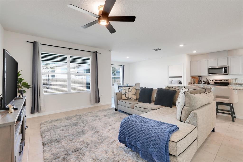 A living room with a sectional sofa, television, and an open kitchen in the background — 11400 AMBER RIDGE DRIVE, ZELLWOOD, FL