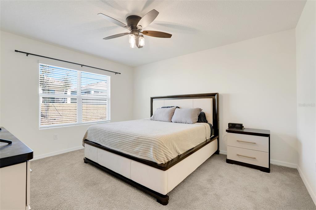 A bedroom features a bed with a dark frame, a nightstand, and a ceiling fan — 11400 AMBER RIDGE DRIVE, ZELLWOOD, FL