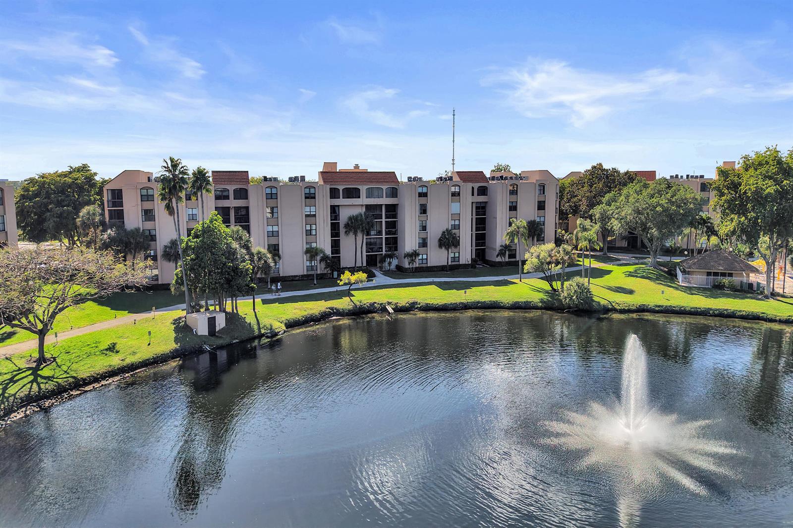 An aerial view shows a multi-story apartment building situated beside a pond with a fountain — 2455 Lindell Boulevard # 3305, Delray Beach FL 33444, DELRAY BEACH, FL