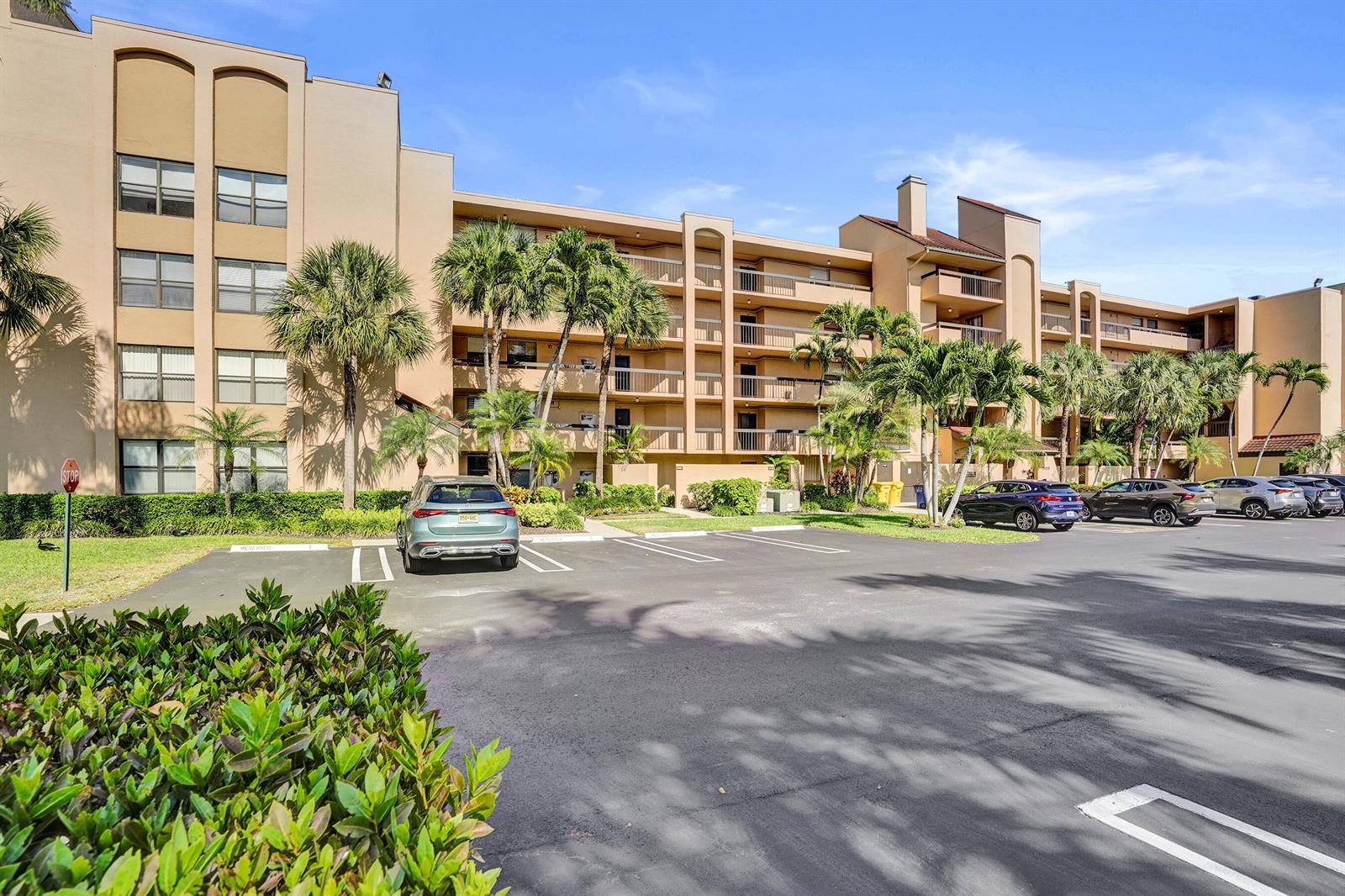 A multi-story apartment building with balconies stands behind a paved parking lot and palm trees — 2455 Lindell Boulevard # 3305, Delray Beach FL 33444, DELRAY BEACH, FL