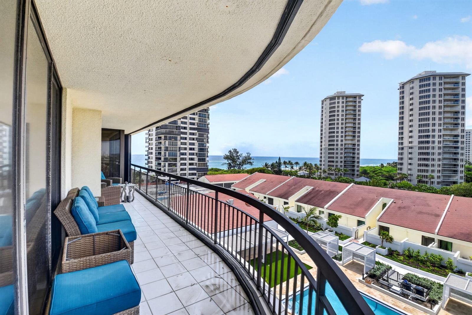 A curved balcony with blue cushioned seating overlooks a swimming pool and the ocean — 4100 N Ocean Drive # 604, Singer Island FL 33404, SINGER ISLAND, FL