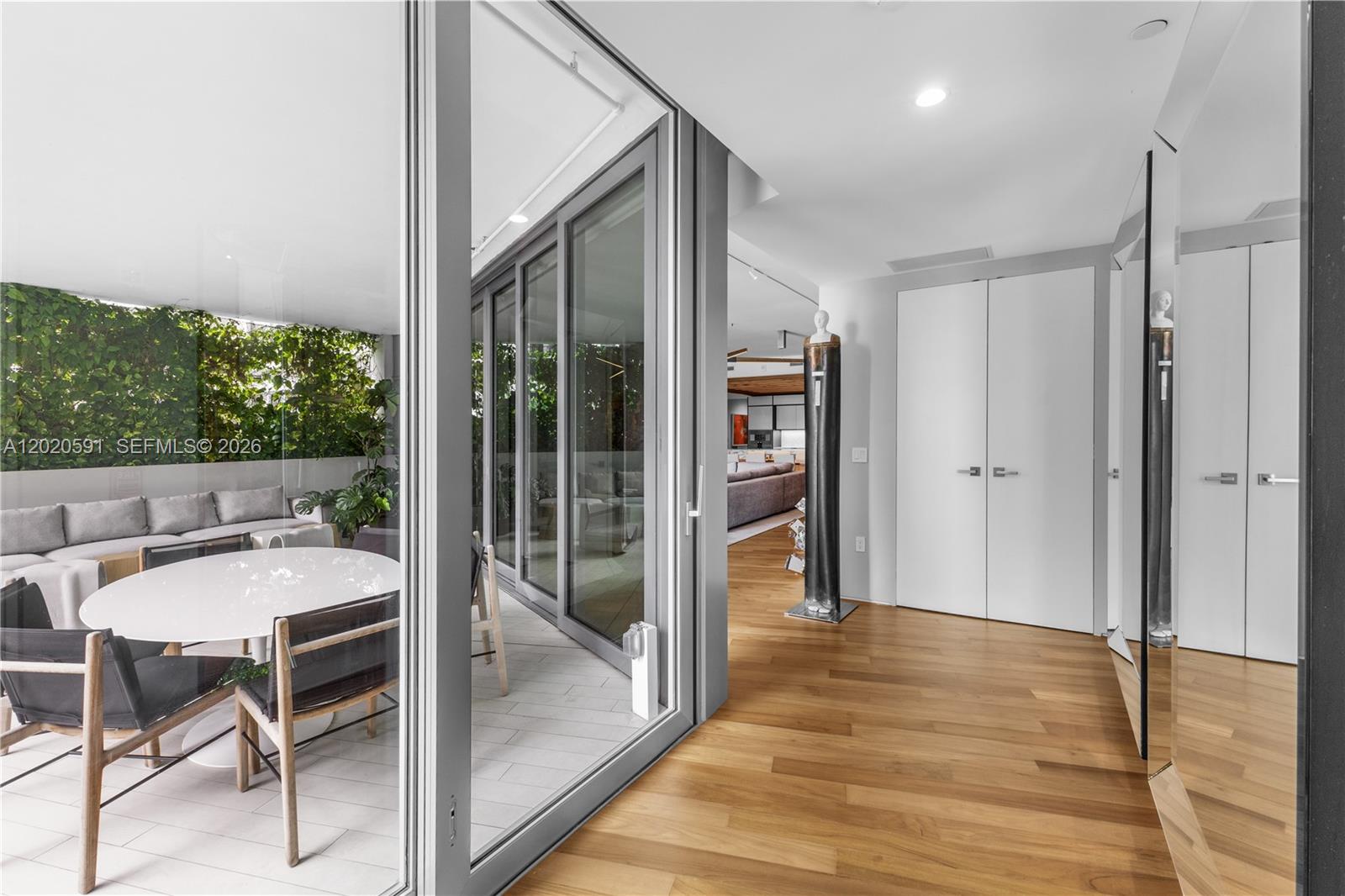 A bright hallway with hardwood floors leads to a glass-enclosed balcony with outdoor seating — 1300 Monad Ter # 3E, Miami Beach FL 33139, MIAMI BEACH, FL