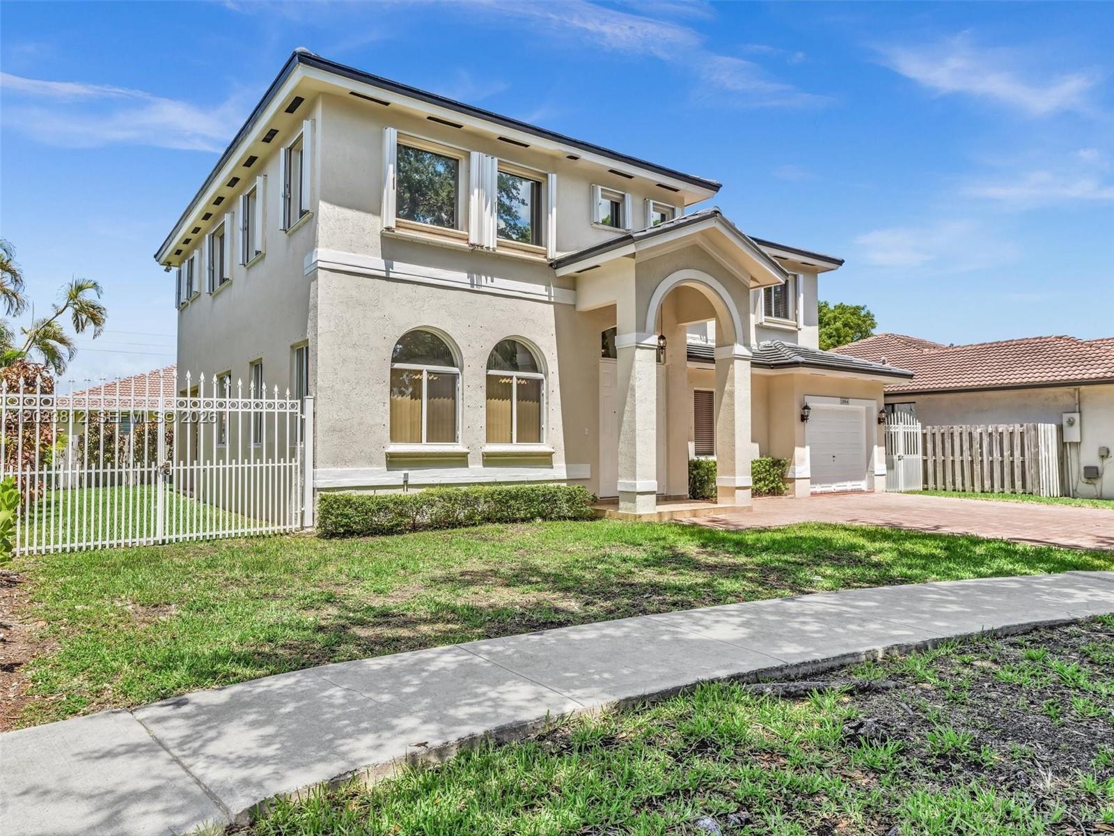 A two-story beige house with an arched entryway, a white fence, and a paved driveway — 2864 SW 138th Path, Miami FL 33175, MIAMI, FL