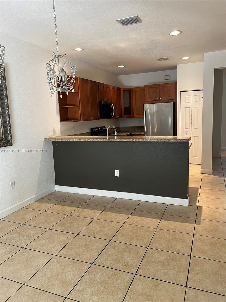 A kitchen features wooden cabinets, stainless steel appliances, and a dark-painted breakfast bar — 11440 NW 75th Ter, Doral FL 33178, DORAL, FL