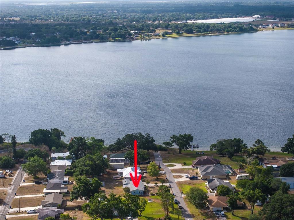 An aerial view shows a blue house with a red arrow pointing toward its roof — 729 E LAKE AVENUE, EAGLE LAKE, FL