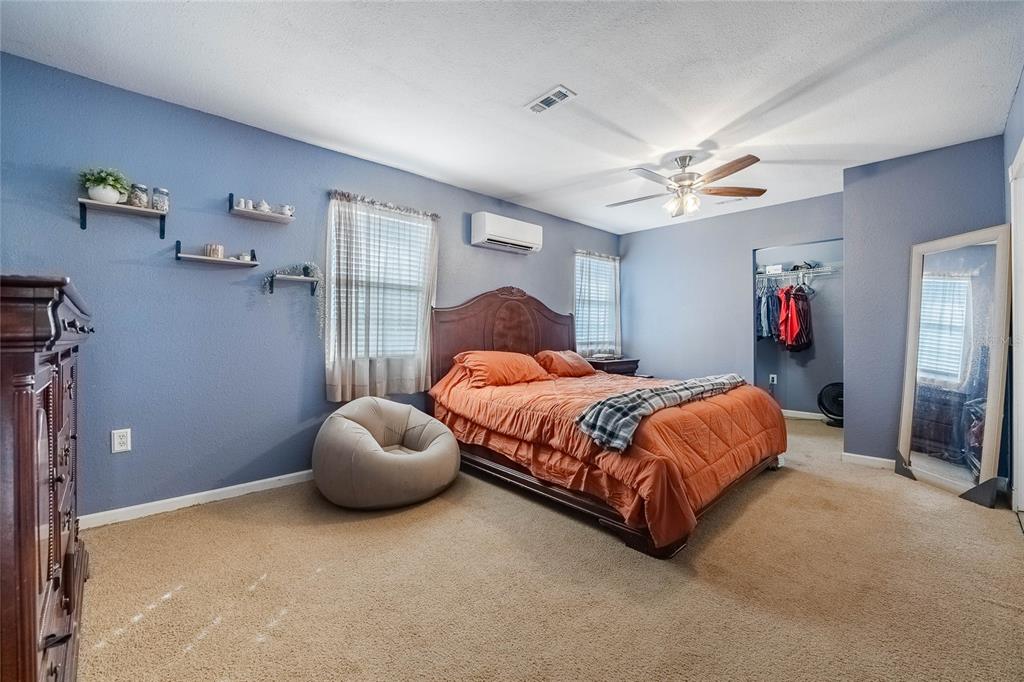 A bedroom features blue walls, a wooden bed frame with orange bedding, and carpeted flooring — 729 E LAKE AVENUE, EAGLE LAKE, FL