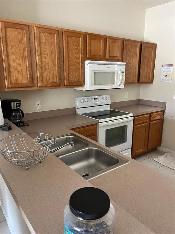 A kitchen features wood cabinets, white appliances, a double sink, and tan countertops — 4529 ALBERTO CIRCLE, KISSIMMEE, FL