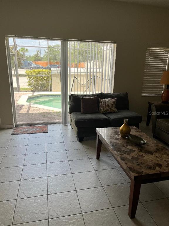 A living room with tiled floors, a dark sofa, and a sliding door to a pool — 4529 ALBERTO CIRCLE, KISSIMMEE, FL