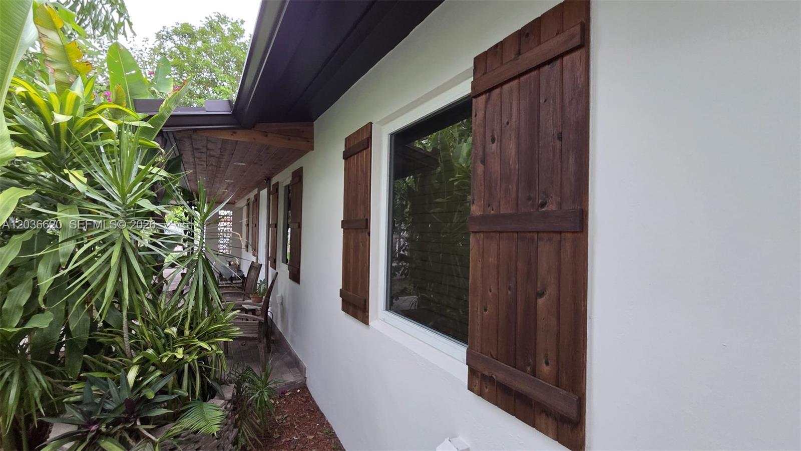 A white exterior wall features dark wood shutters flanking a window along a covered porch — 3511 SW 105th ct, Miami FL 33165, MIAMI, FL