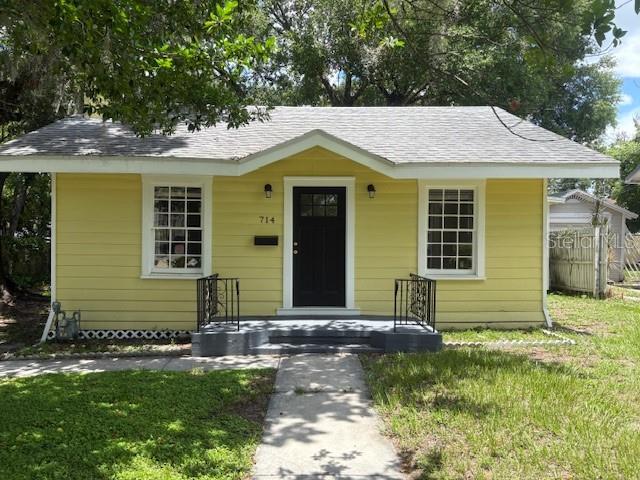 A yellow, single-story house with a dark front door and a gray shingled roof — 714 WINFREE AVENUE, LAKELAND, FL