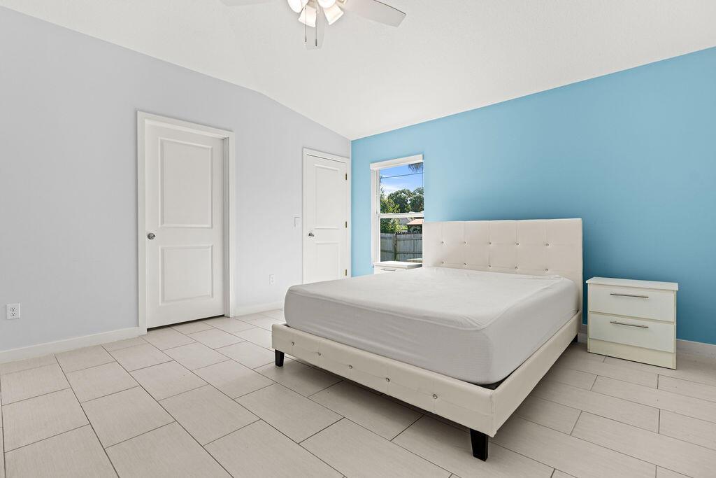 A bedroom features light blue and white walls, tile flooring, and a white upholstered bed — 1022 41st Avenue, Vero Beach FL 32960, VERO BEACH, FL