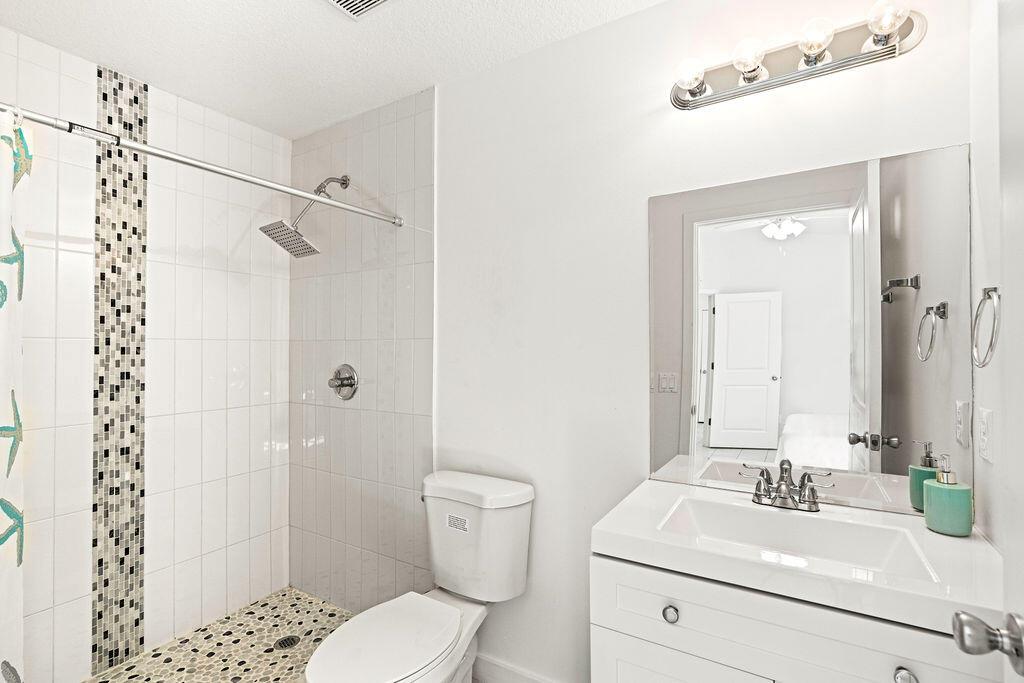 A bathroom features a white vanity, a toilet, and a walk-in shower with pebble flooring — 1022 41st Avenue, Vero Beach FL 32960, VERO BEACH, FL