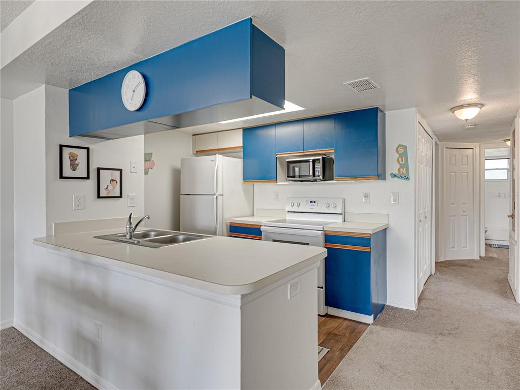 A kitchen features blue cabinets, white appliances, a breakfast bar, and a wall-mounted clock — 2729 N POINCIANA BOULEVARD UNIT 125, KISSIMMEE, FL