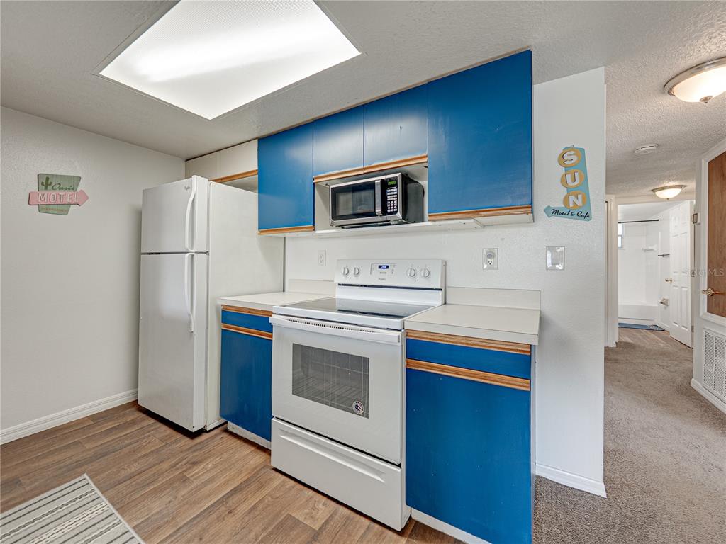 A kitchen features blue cabinets, white appliances, and wood-look flooring — 2729 N POINCIANA BOULEVARD UNIT 125, KISSIMMEE, FL