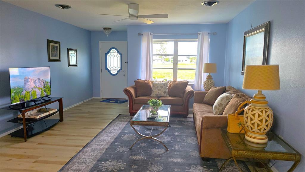 A living room features blue walls, light wood flooring, a ceiling fan, and brown furniture — 199 CADDY ROAD, ROTONDA WEST, FL