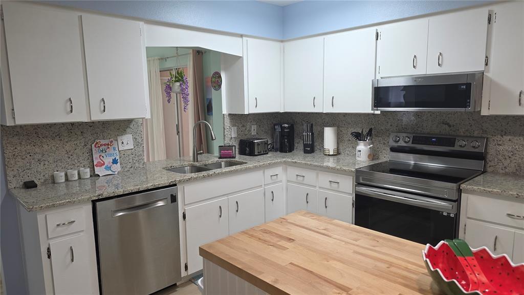 A kitchen with white cabinets, granite countertops, stainless steel appliances, and a wood-topped island — 199 CADDY ROAD, ROTONDA WEST, FL