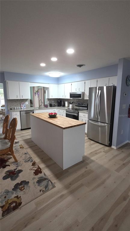 A kitchen features white cabinetry, a wood-topped island, stainless steel appliances, and light wood flooring — 199 CADDY ROAD, ROTONDA WEST, FL