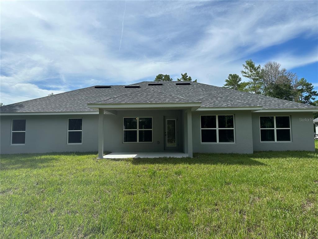 The rear exterior of a single-story gray house features a covered patio and lawn — 12126 PINE WARBLER AVENUE, BROOKSVILLE, FL