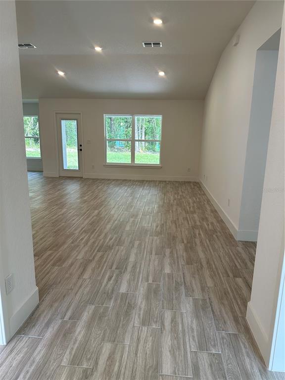 An open living area features light wood-look tile flooring, recessed lighting, and a glass-paneled door — 12126 PINE WARBLER AVENUE, BROOKSVILLE, FL
