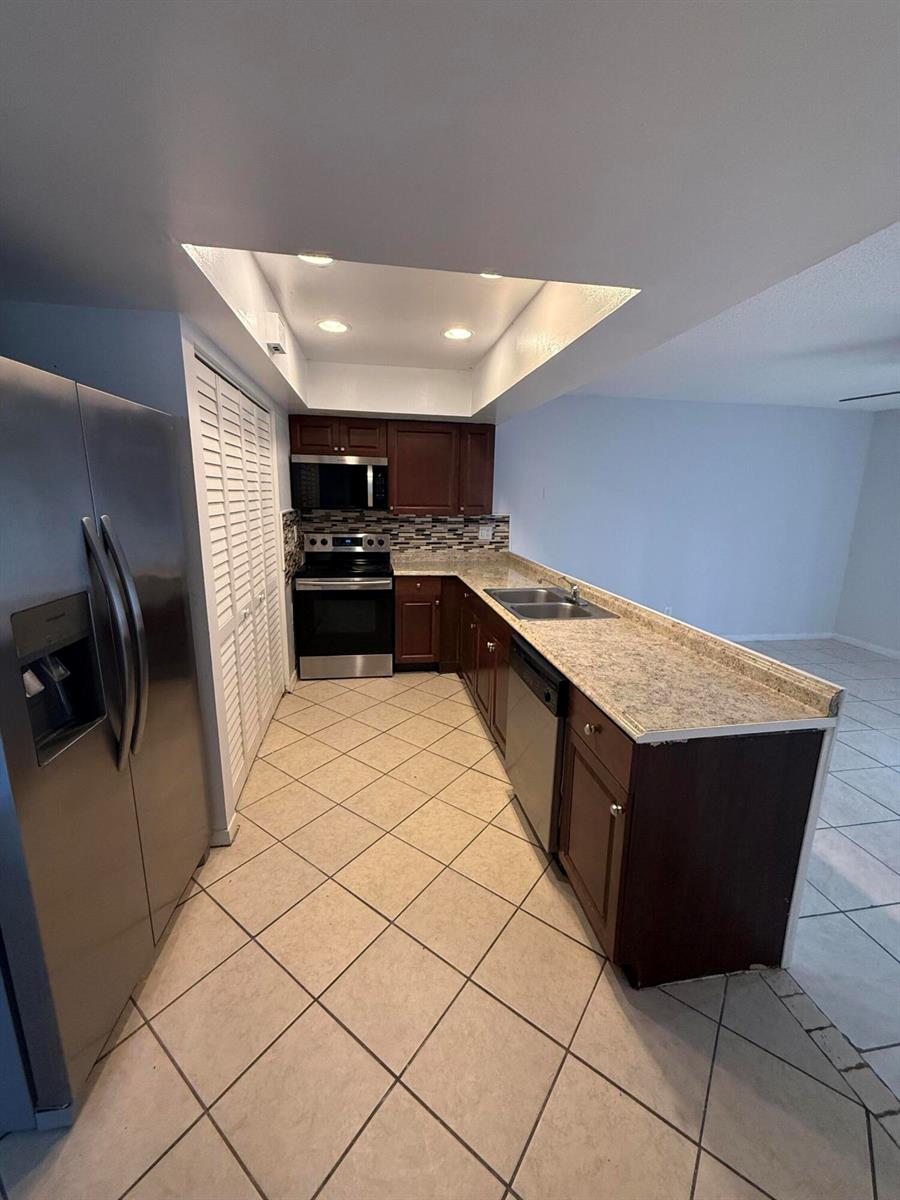 A kitchen features dark wood cabinets, granite countertops, stainless steel appliances, and diagonal tile flooring — 1201 White Pine Drive # 1201, Wellington FL 33414, WELLINGTON, FL