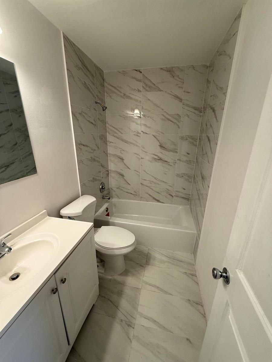 A bathroom features a white vanity, a toilet, and a bathtub with marble-patterned tile walls — 1201 White Pine Drive # 1201, Wellington FL 33414, WELLINGTON, FL