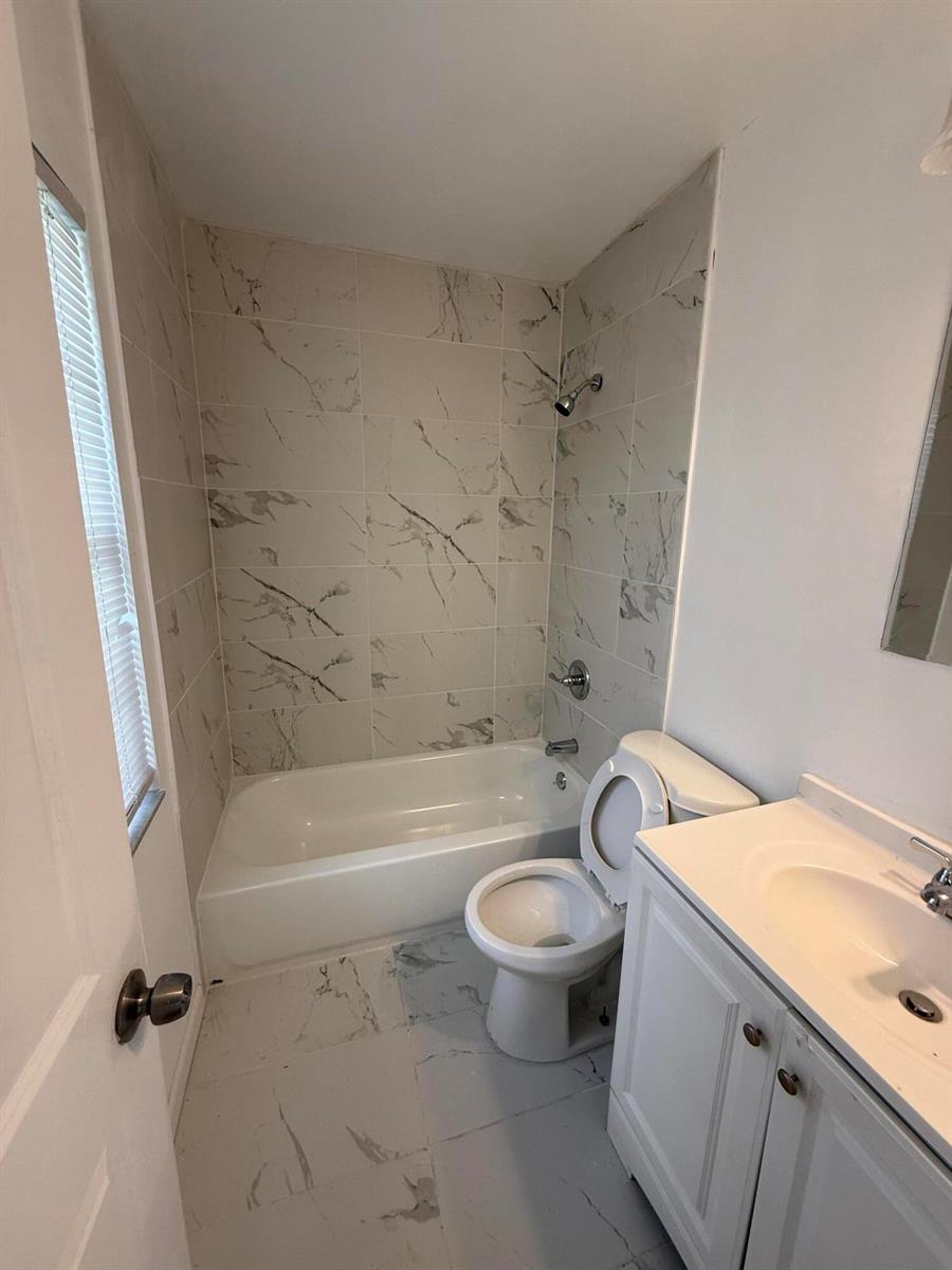 A bathroom features a white vanity, a toilet, and a bathtub with marble-patterned tile walls — 1201 White Pine Drive # 1201, Wellington FL 33414, WELLINGTON, FL