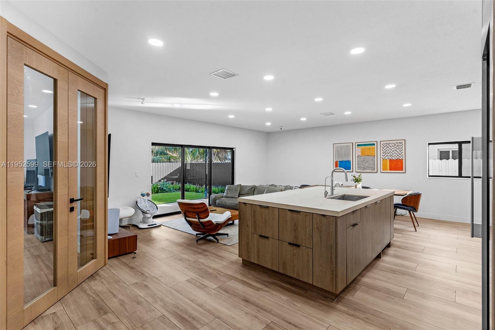 A modern open-concept kitchen and living area features a large island and wood-look flooring — 15619 SW 14th St, Miami FL 33194, MIAMI, FL