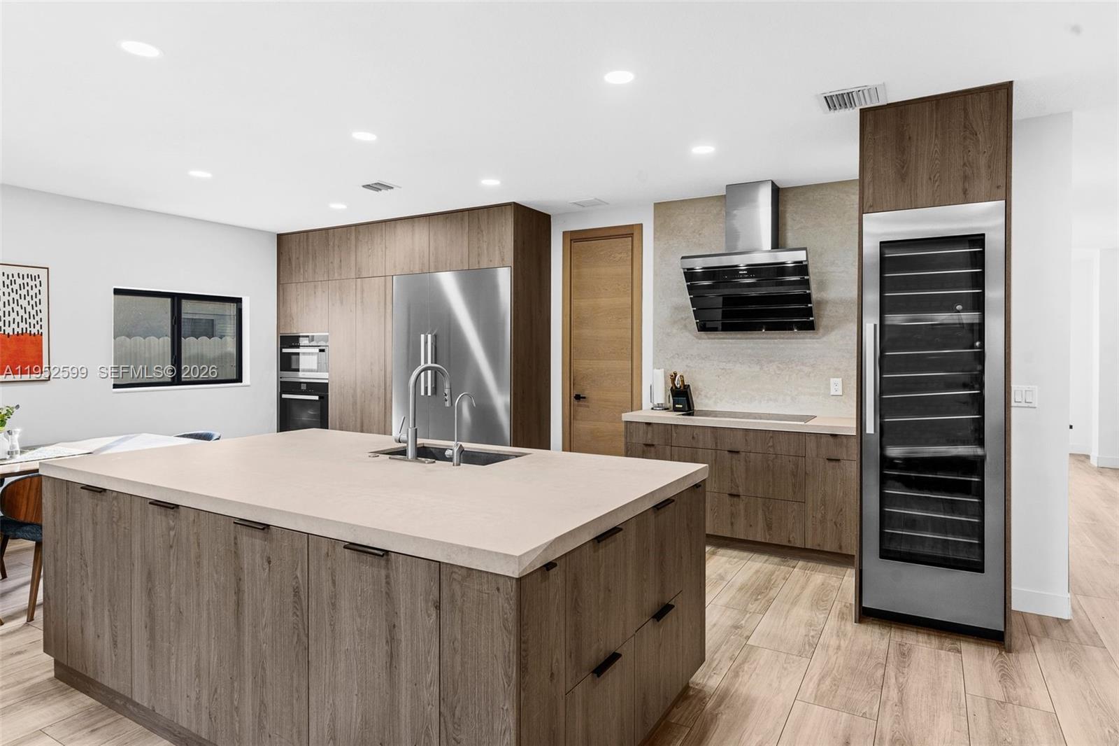 A modern kitchen features wood-grain cabinetry, a large island with a sink, and stainless appliances — 15619 SW 14th St, Miami FL 33194, MIAMI, FL