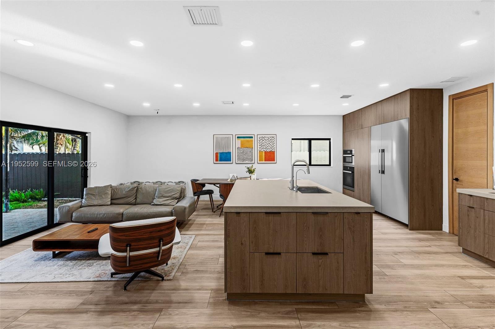 This open-concept kitchen and living area features wood cabinetry, a central island, and sliding doors — 15619 SW 14th St, Miami FL 33194, MIAMI, FL