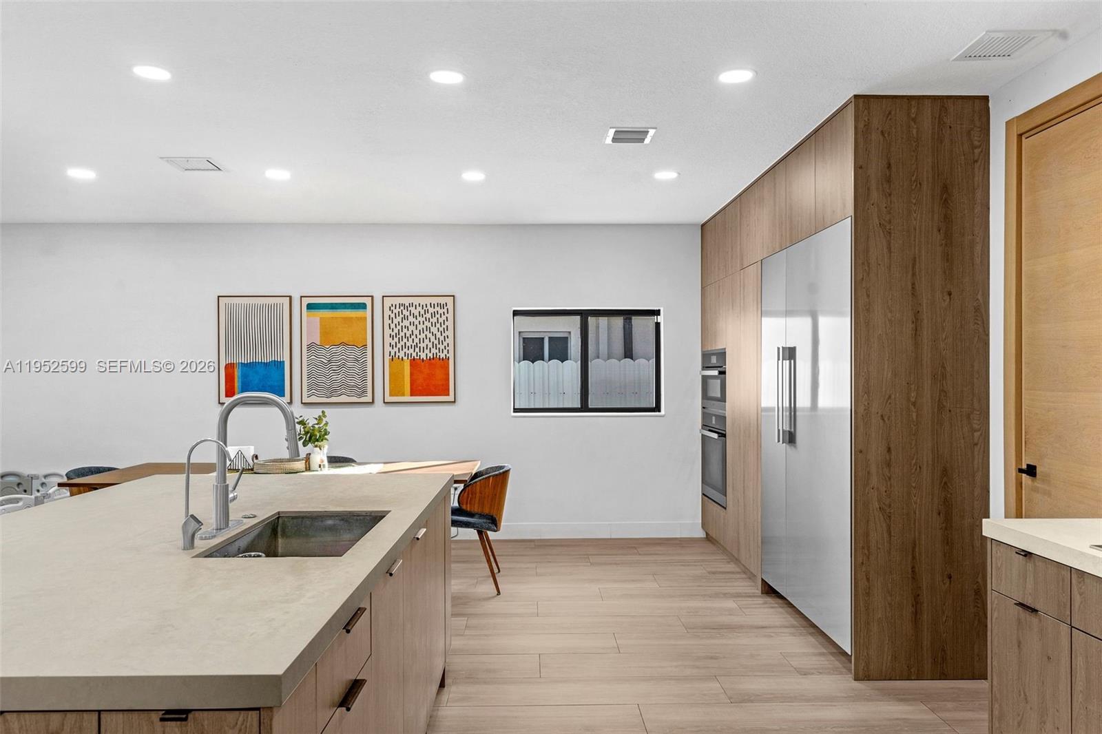 A modern kitchen features a large island, light wood cabinetry, and three framed wall prints — 15619 SW 14th St, Miami FL 33194, MIAMI, FL