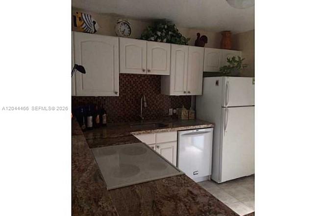 A kitchen features white cabinets, granite countertops, a glass cooktop, and a white refrigerator — AVENTURA, FL