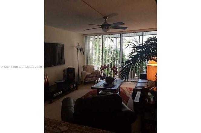 A living room features a ceiling fan, a television, and large windows with vertical blinds — AVENTURA, FL