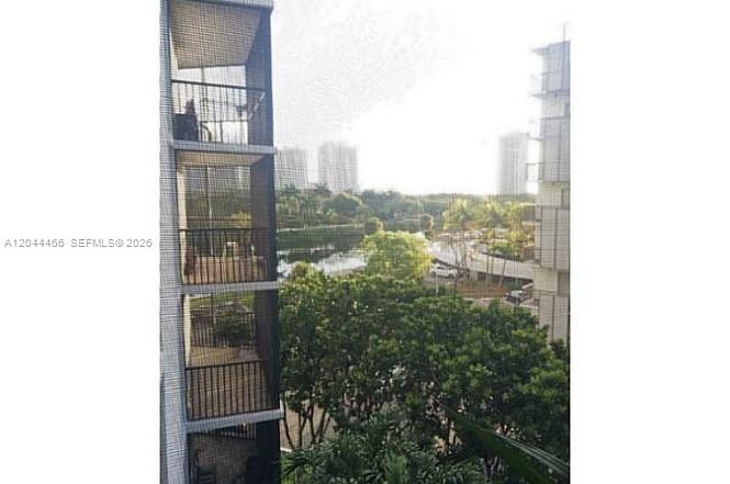 A view from a high-rise balcony overlooking trees, a small pond, and distant buildings — AVENTURA, FL