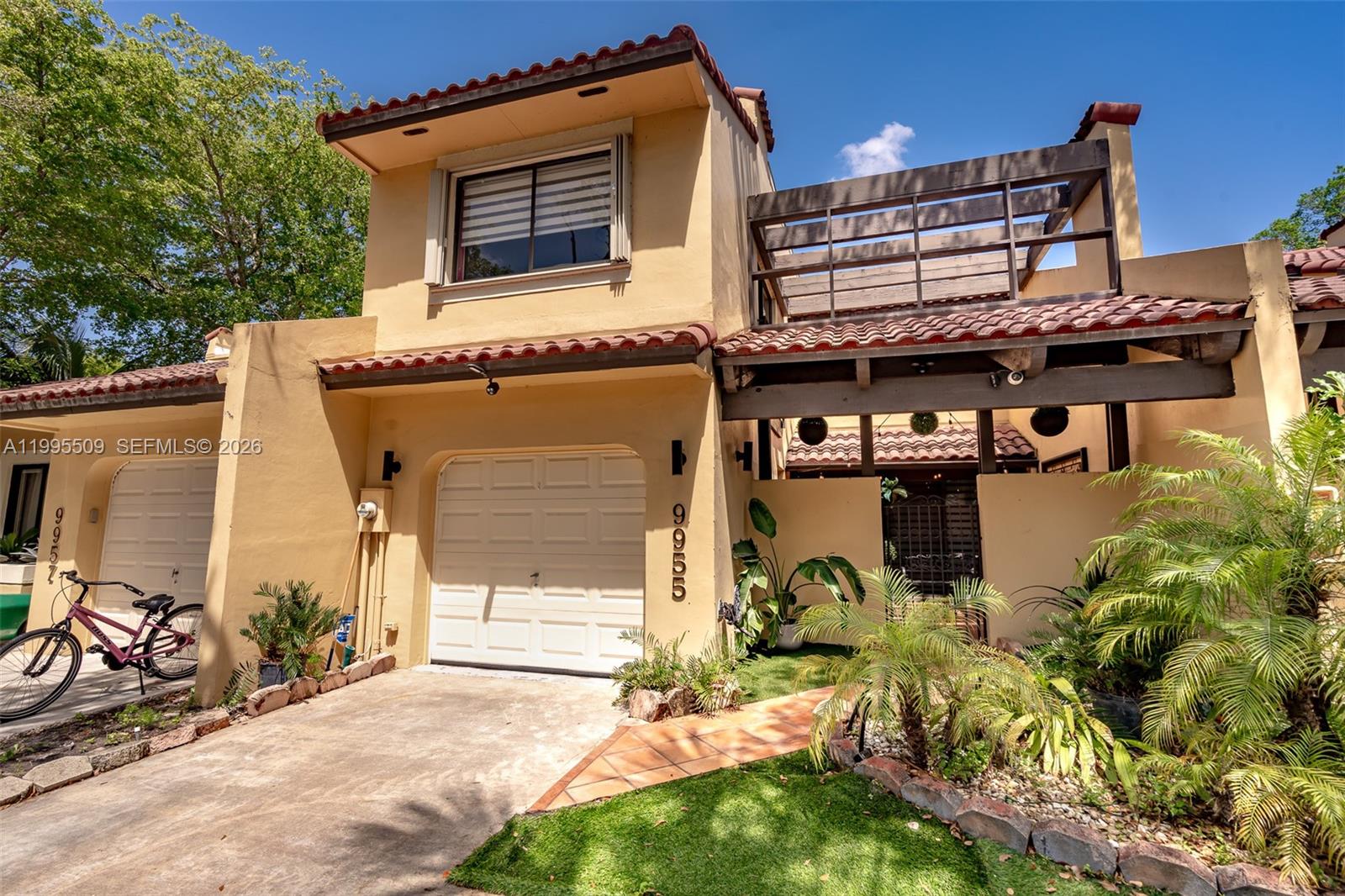 A two-story tan stucco townhouse features a garage, a tiled entryway, and a wooden pergola — 9955 Costa Del Sol Blvd # 108B, Doral FL 33178, DORAL, FL