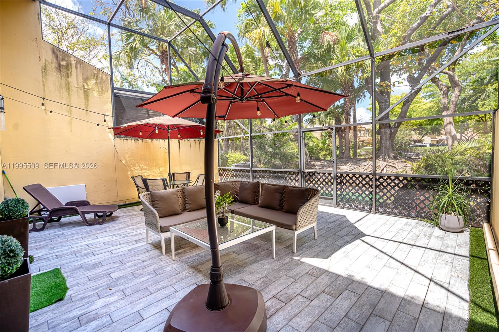A screened-in patio features a sectional sofa, a glass coffee table, and two red umbrellas — 9955 Costa Del Sol Blvd # 108B, Doral FL 33178, DORAL, FL