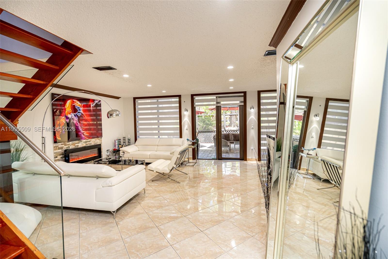 A modern living room features white leather sofas, a fireplace, and a staircase — 9955 Costa Del Sol Blvd # 108B, Doral FL 33178, DORAL, FL