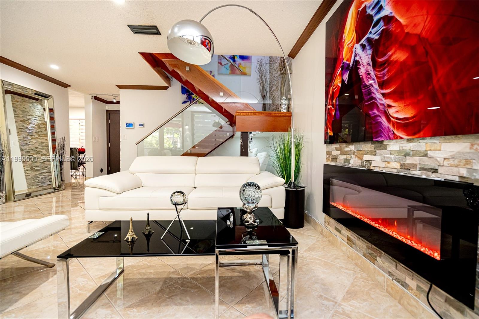 A modern living room features a white sofa, glass coffee tables, and a wall-mounted fireplace — 9955 Costa Del Sol Blvd # 108B, Doral FL 33178, DORAL, FL
