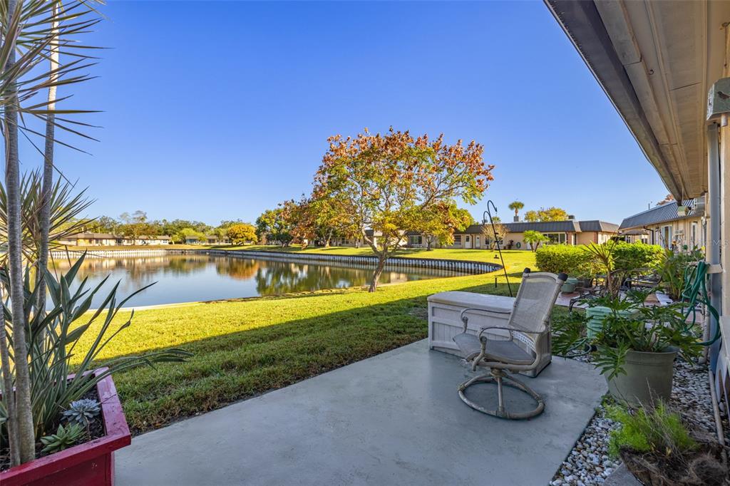 A concrete patio overlooks a grassy lawn and a small lake behind a residential building — 4324 SUMMERSUN DRIVE, NEW PORT RICHEY, FL