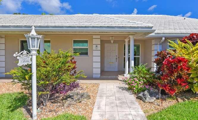 The exterior of a single-story house features a white tiled roof, columns, and landscaping — 437 French Royale Circle, Atlantis FL 33462, ATLANTIS, FL