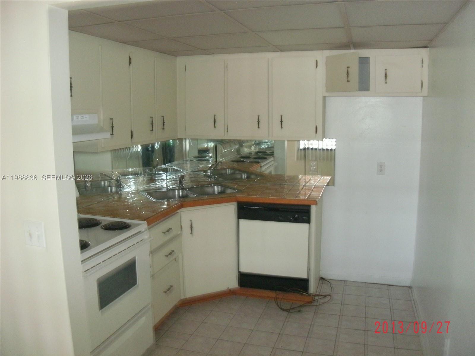 A kitchen features white cabinets, tiled countertops, a mirrored backsplash, and a black dishwasher — 1409 Lake Ave # 5, Lake Worth FL 33460, LAKE WORTH, FL