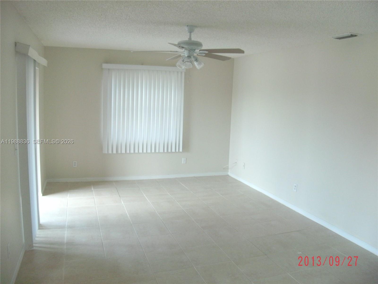 An empty living room features beige tile flooring, light-colored walls, a ceiling fan, and vertical blinds — 1409 Lake Ave # 5, Lake Worth FL 33460, LAKE WORTH, FL